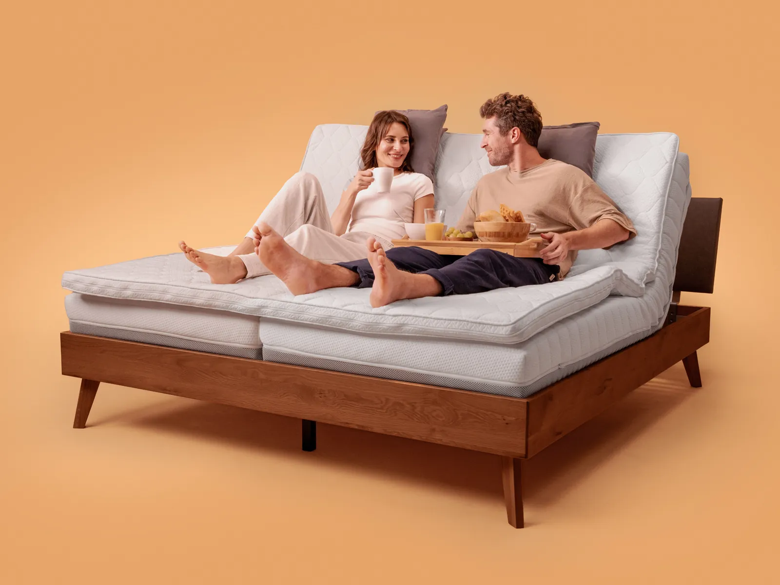 Un couple assis dans un grand lit, les deux côtés relevés ensemble par le CosyLift Bundle Sync